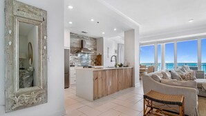 A spacious living area with a large window overlooking the ocean, a wooden island in the kitchen, and a mirror with decorative elements. - La Playa 402 (Pensacola)