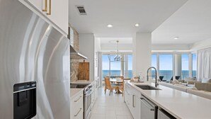 A modern kitchen with a stainless steel refrigerator, white cabinetry, and a dining area with a view of the ocean. - La Playa 402 (Pensacola)