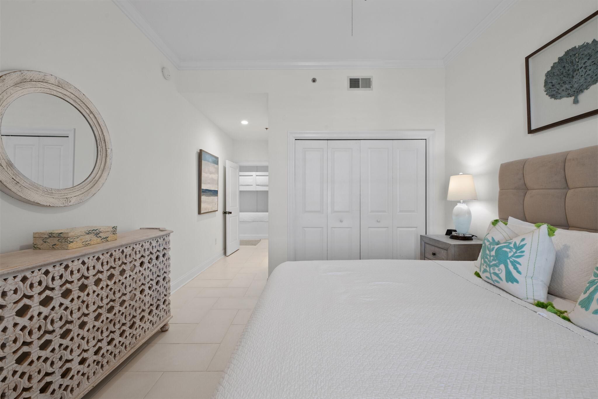 Une chambre à coucher comprenant un lit, une table de chevet, une commode, un miroir et une porte donnant sur une salle de bain.