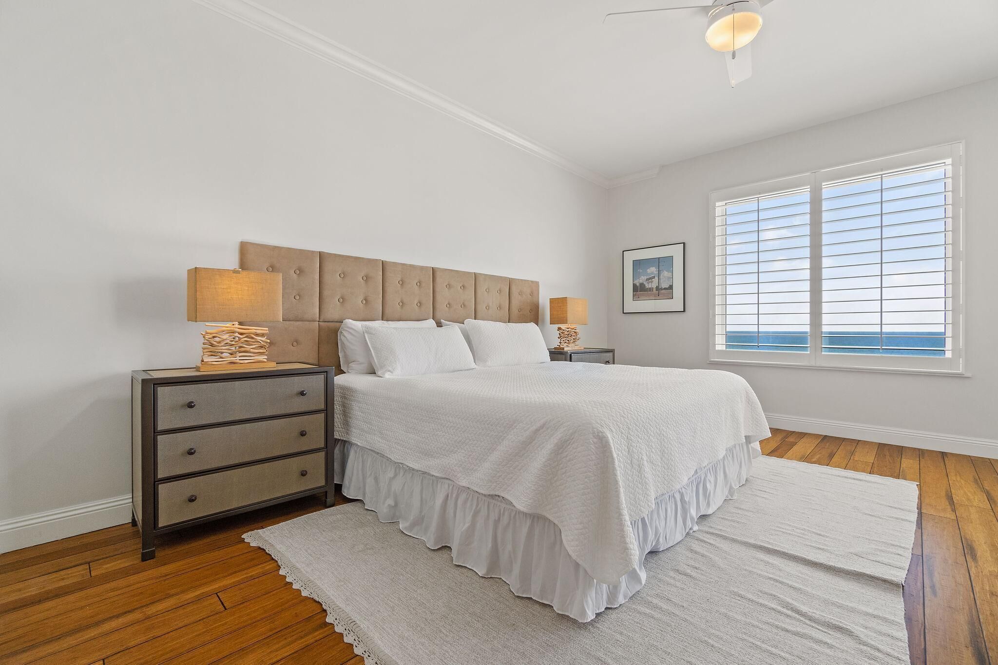 A bedroom with a bed, two nightstands, a lamp, a window, and a wooden floor.