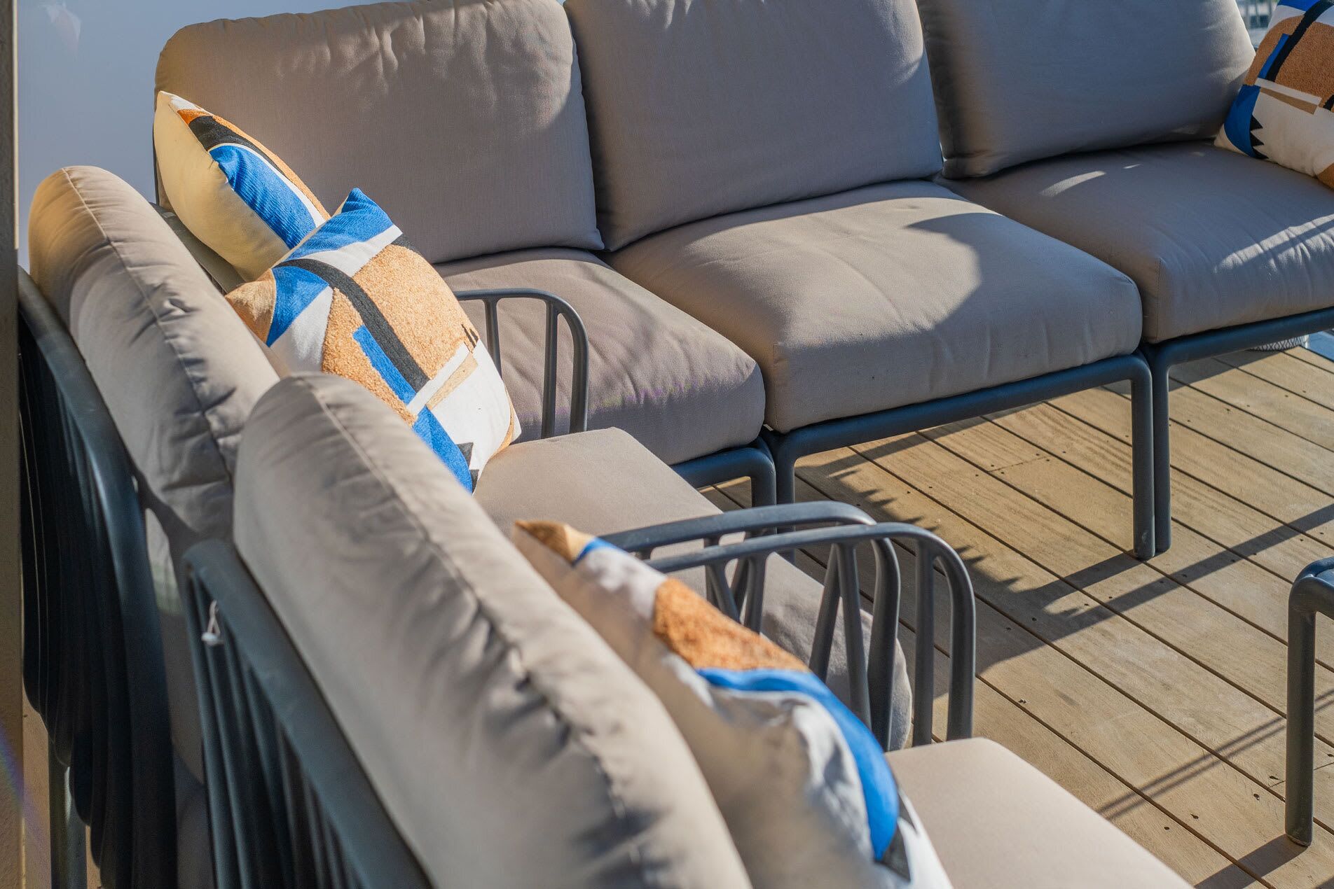 A row of beige cushioned outdoor seating with metal frames, arranged on a wooden deck.