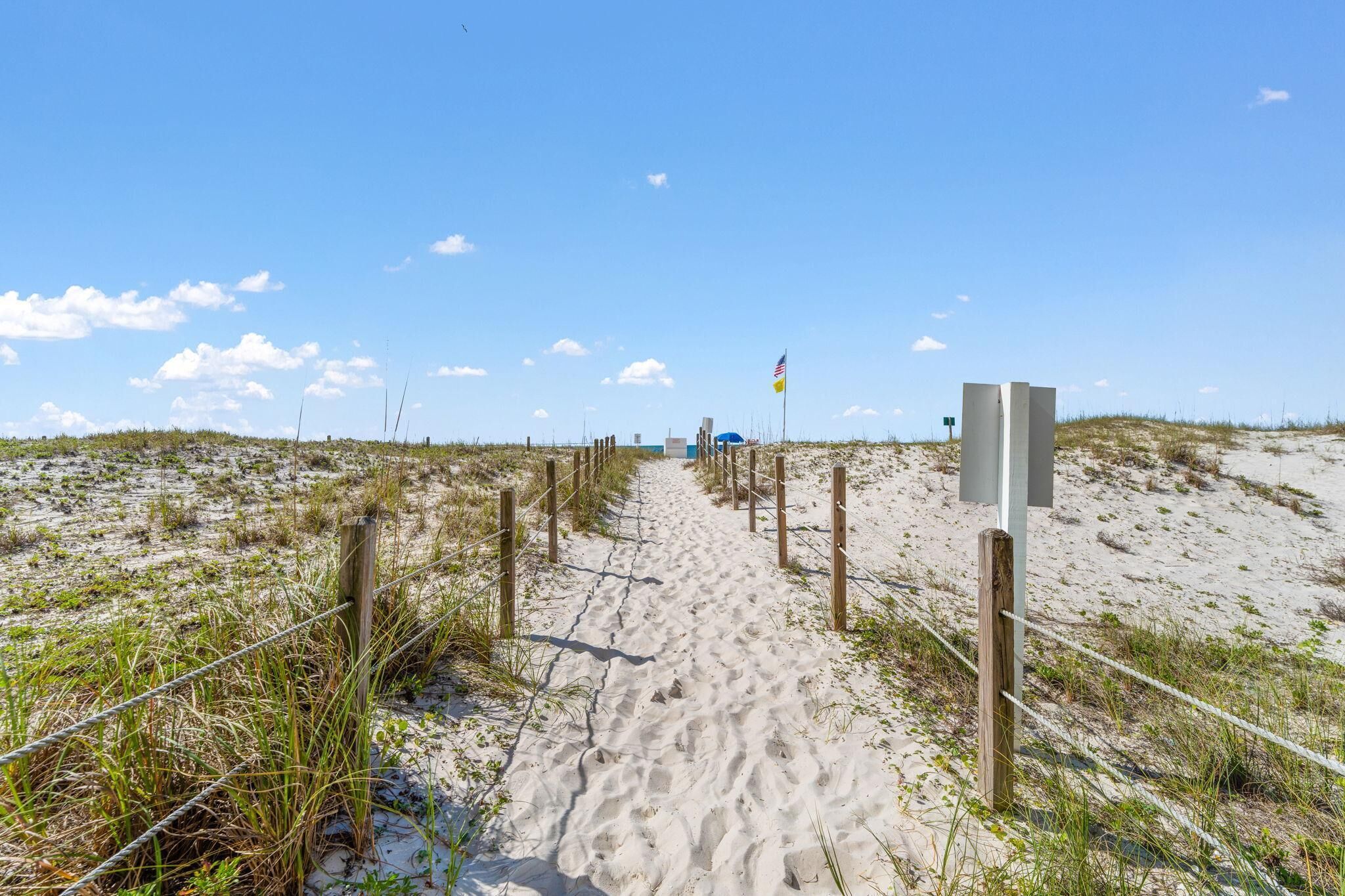 Ein Sandweg am Strand mit Holzbefestigung und einem blauen Sonnenschirm.