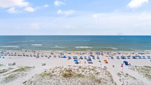 A beach with numerous umbrellas and beach chairs, sandy terrain, and the ocean in the background. - Castaways 7B (Gulf Shores)