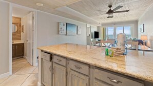 A modern kitchen with granite countertops, wooden cabinets, and a ceiling fan. - Castaways 7B (Gulf Shores)