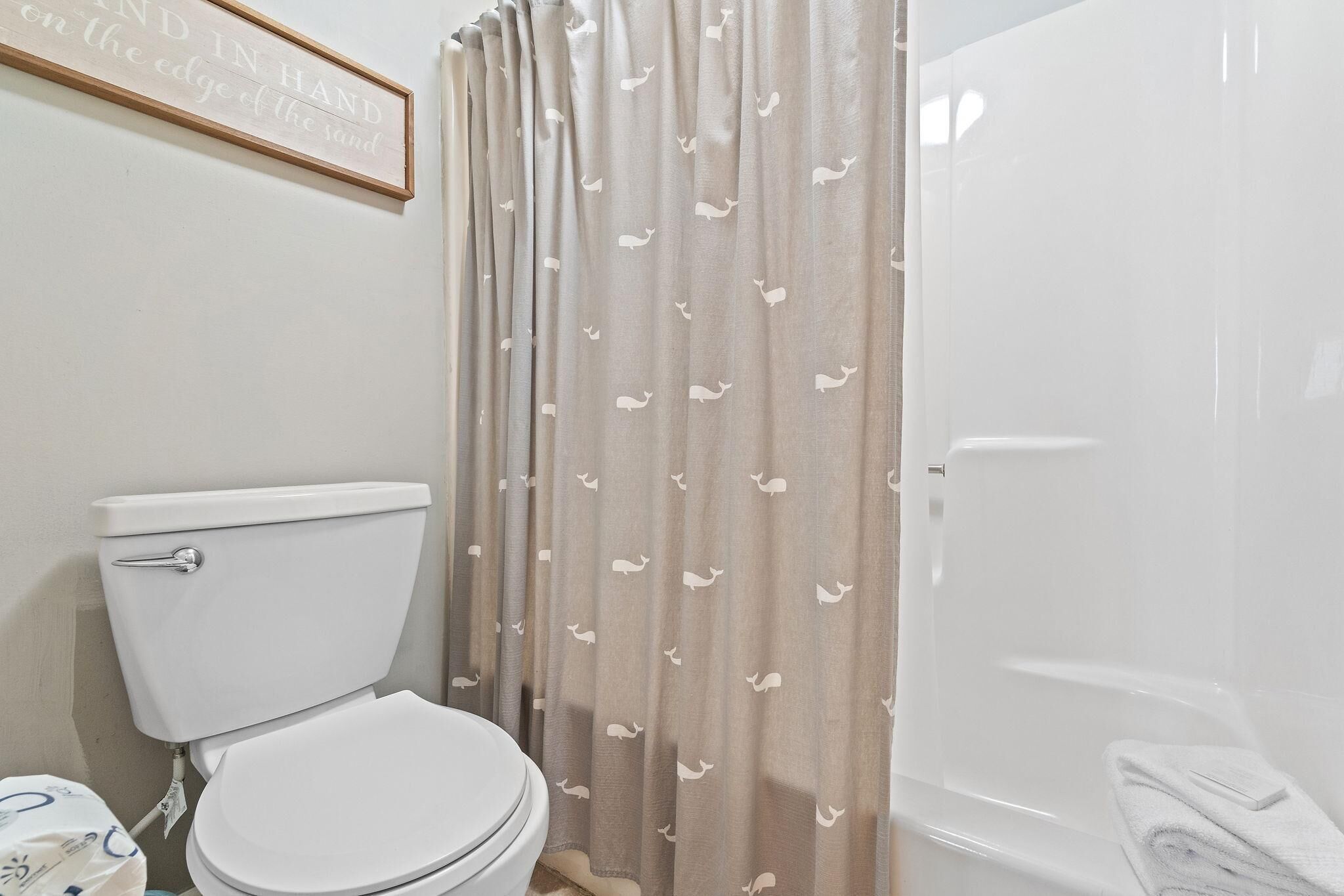 A bathroom with a toilet, a shower curtain with a pattern, and a framed quote on the wall.