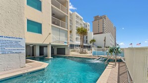 A swimming pool with a lifeguard sign, poolside area, and a multi-story building in the background. - Castaways 7B (Gulf Shores)