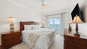 A bedroom with a large bed, two bedside tables with lamps, a ceiling fan, and a view of the ocean through a balcony. - Seawind 1302 (Gulf Shores)