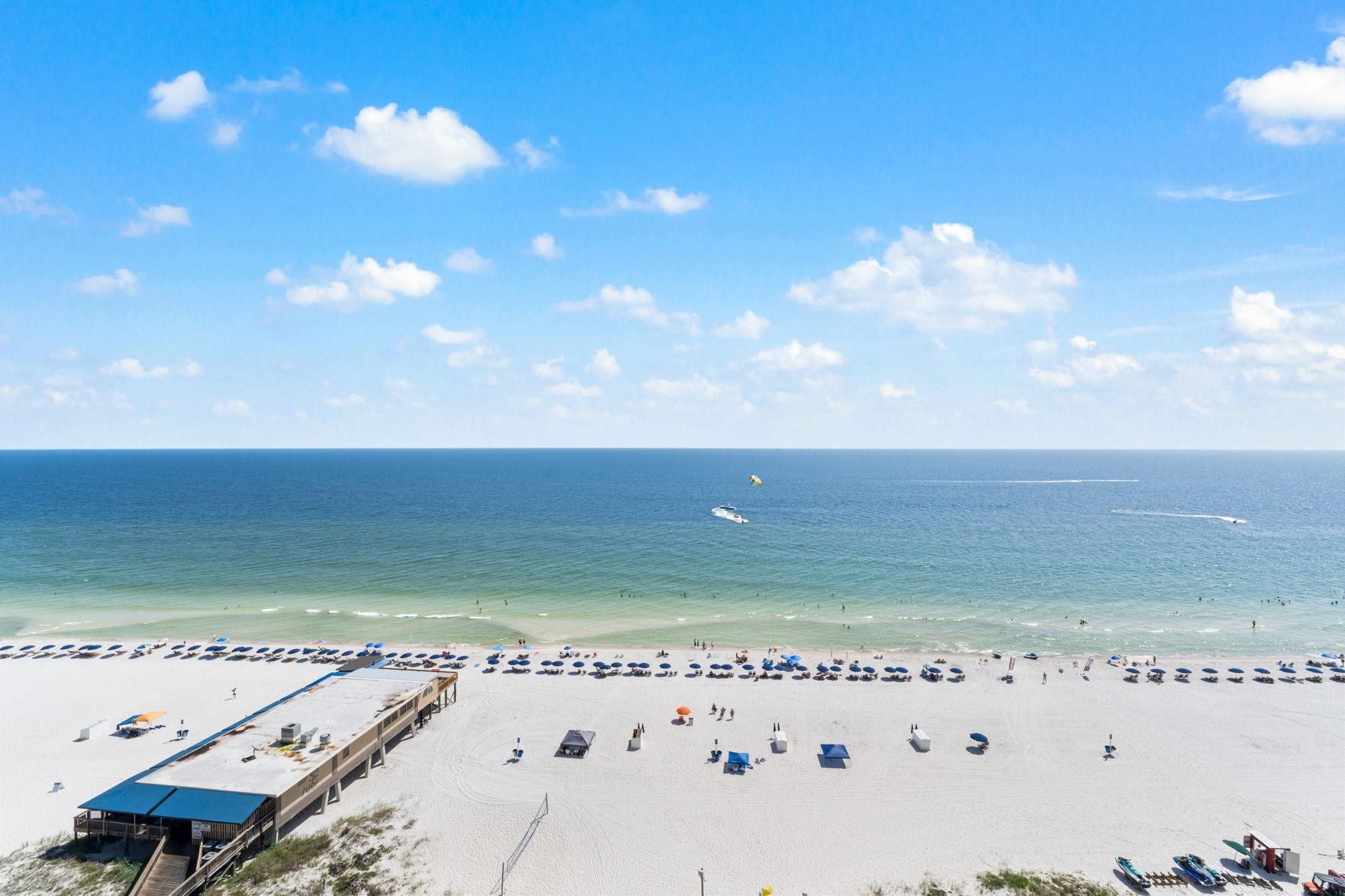 A beach with a pier, umbrellas, and a clear sky.