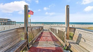 A wooden boardwalk leading to a beach with a flag on the left and a building on the right. - Seawind 1302 (Gulf Shores)