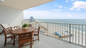 A balcony with a wooden table and chairs, a potted plant, and a view of the beach and ocean. - Seawind 1302 (Gulf Shores)