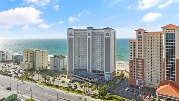 A high-rise hotel with multiple balconies, a parking lot, and a view of the ocean. - Seawind 1302 (Gulf Shores)