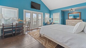 A bedroom with a large bed, a TV mounted on the wall, and a ceiling fan. - The Last Mango (Gulf Shores)