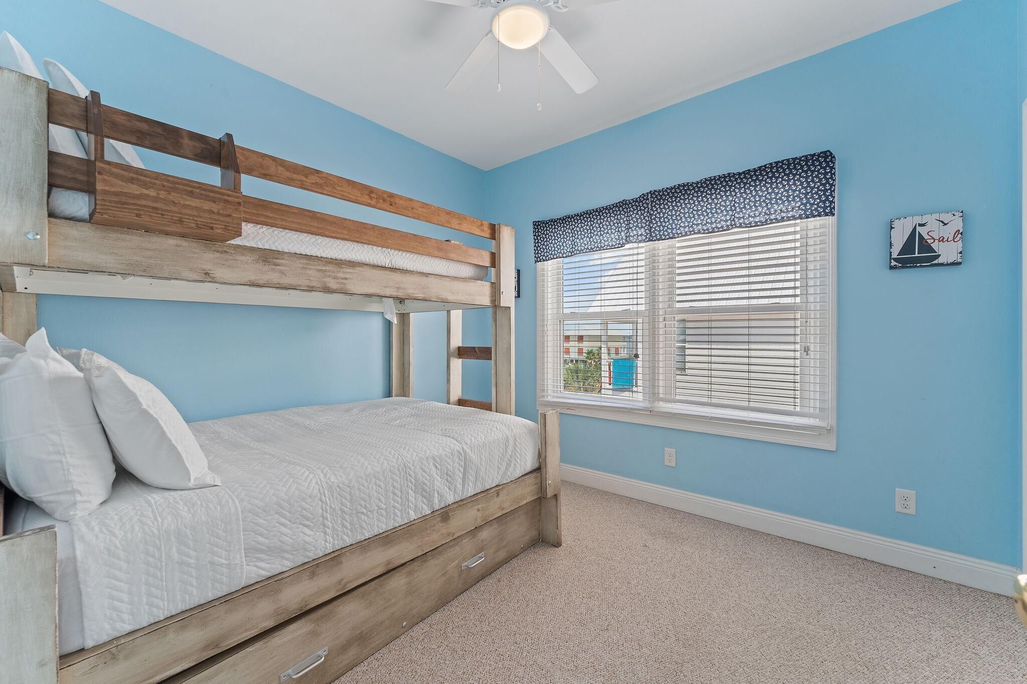 Una cama litera con estructura de madera y ropa de cama blanca, un ventilador de techo y una ventana con persianas.