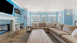A living room with a sectional sofa, a flat-screen TV, a fireplace, and a ceiling fan. - The Last Mango (Gulf Shores)