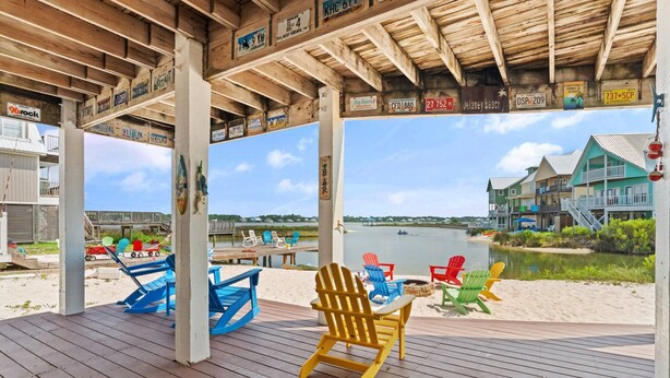 A wooden deck with Adirondack chairs and a view of a beach and water. - The Last Mango (Gulf Shores)