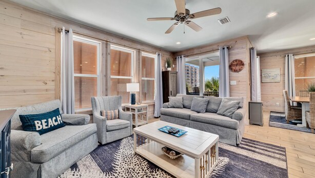 A spacious living room with a large window, a ceiling fan, and a view of the outside. - Romeo Beach Cottage 6 (Gulf Shores)