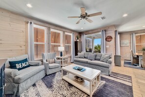 A spacious living room with a large window, a ceiling fan, and a view of the outside. - Romeo Beach Cottage 6 (Gulf Shores)