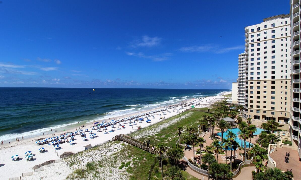 A beach resort with a pool, beach umbrellas, and a high-rise building.