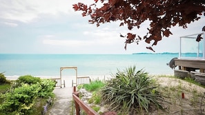 A coastal view with a wooden pathway leading to a beach, a clear sky, and a distant island.