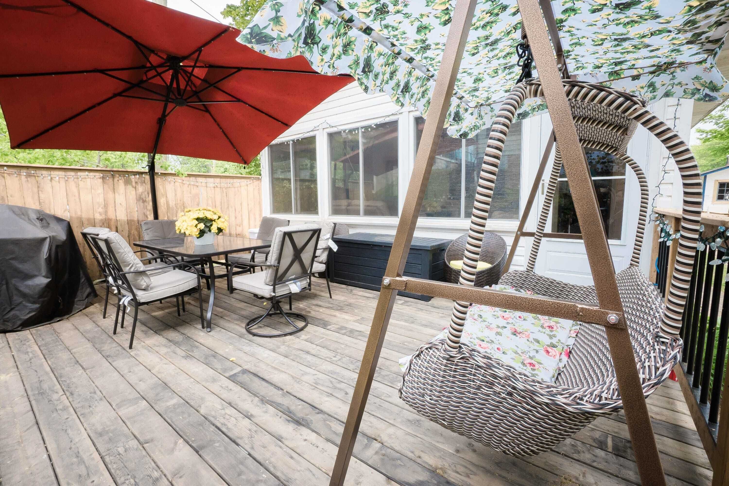 A wooden deck with outdoor furniture, including a table and chairs, a swing chair, and a red umbrella.