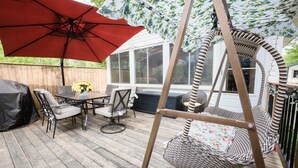 A wooden deck with outdoor furniture, including a table and chairs, a swing chair, and a red umbrella. - Cottage Beside Crystal Beach - 3BR & BBQ! (Fort Erie)