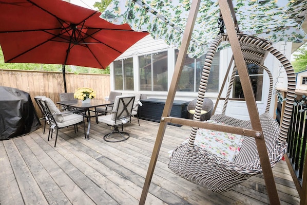 A wooden deck with outdoor furniture, including a table and chairs, a swing chair, and a red umbrella.
