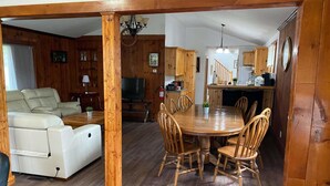 A cozy living room with a sofa, a dining table with chairs, wooden flooring, and a kitchen area with wooden cabinets and a staircase. - Cottage Beside Crystal Beach - 3BR & BBQ! (Fort Erie)