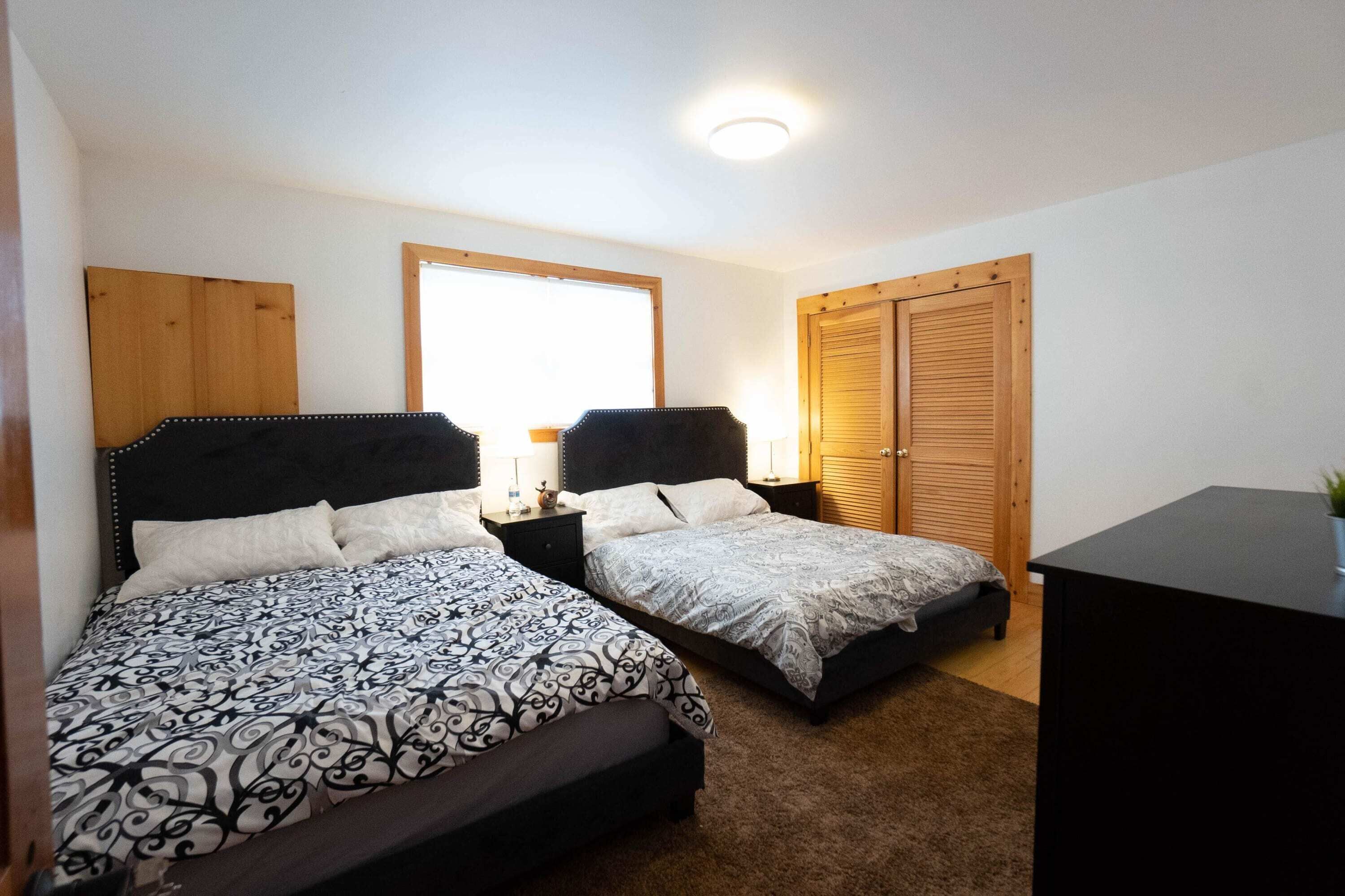 Quarto com duas camas, uma escrivaninha e uma janela.