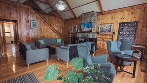 Un intérieur en bois avec un escalier, des canapés gris, un piano et un mur orné d’une affiche représentant un paysage urbain.