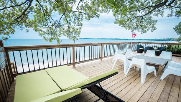 Une terrasse en bois avec une table et des chaises, un banc vert avec coussin, et une vue sur la mer.