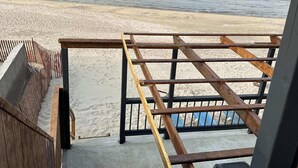 Un escalier en bois menant à une plage de sable, avec une rampe en métal et une vue sur la mer.