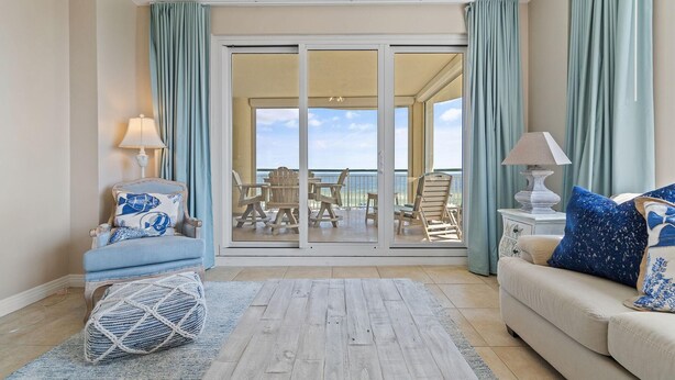 A room with a sofa, armchair, and a table with chairs. There is a view of the ocean through large glass doors. - Beach Colony Tower 4D (Pensacola)