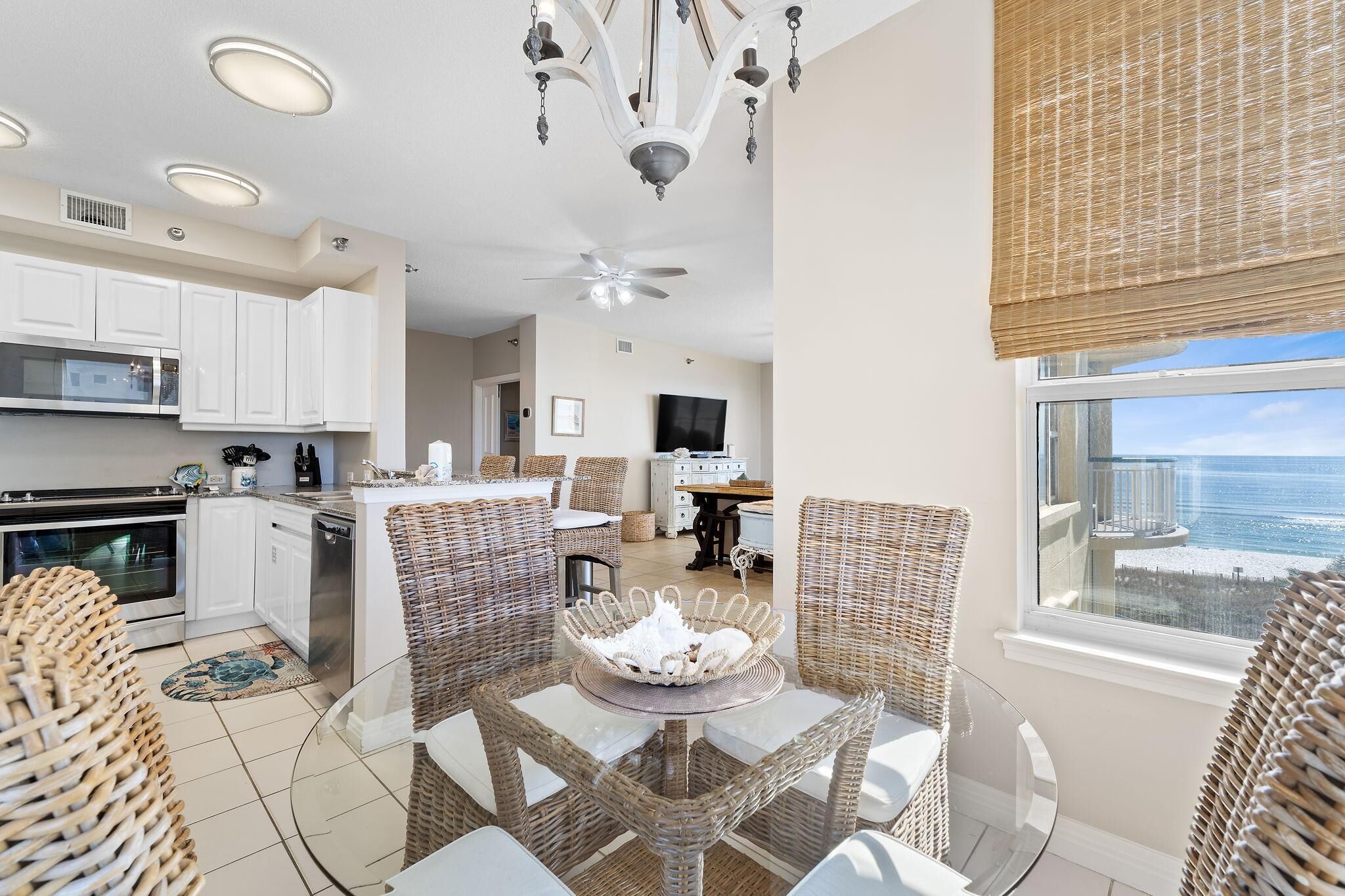 A modern kitchen with white cabinets, a dining area with wicker furniture, and a view of the ocean through a large window.