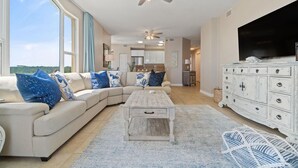 A spacious living room with a large sectional sofa, a wooden coffee table, a white dresser, and a flat-screen TV. - Beach Colony Tower 4D (Pensacola)