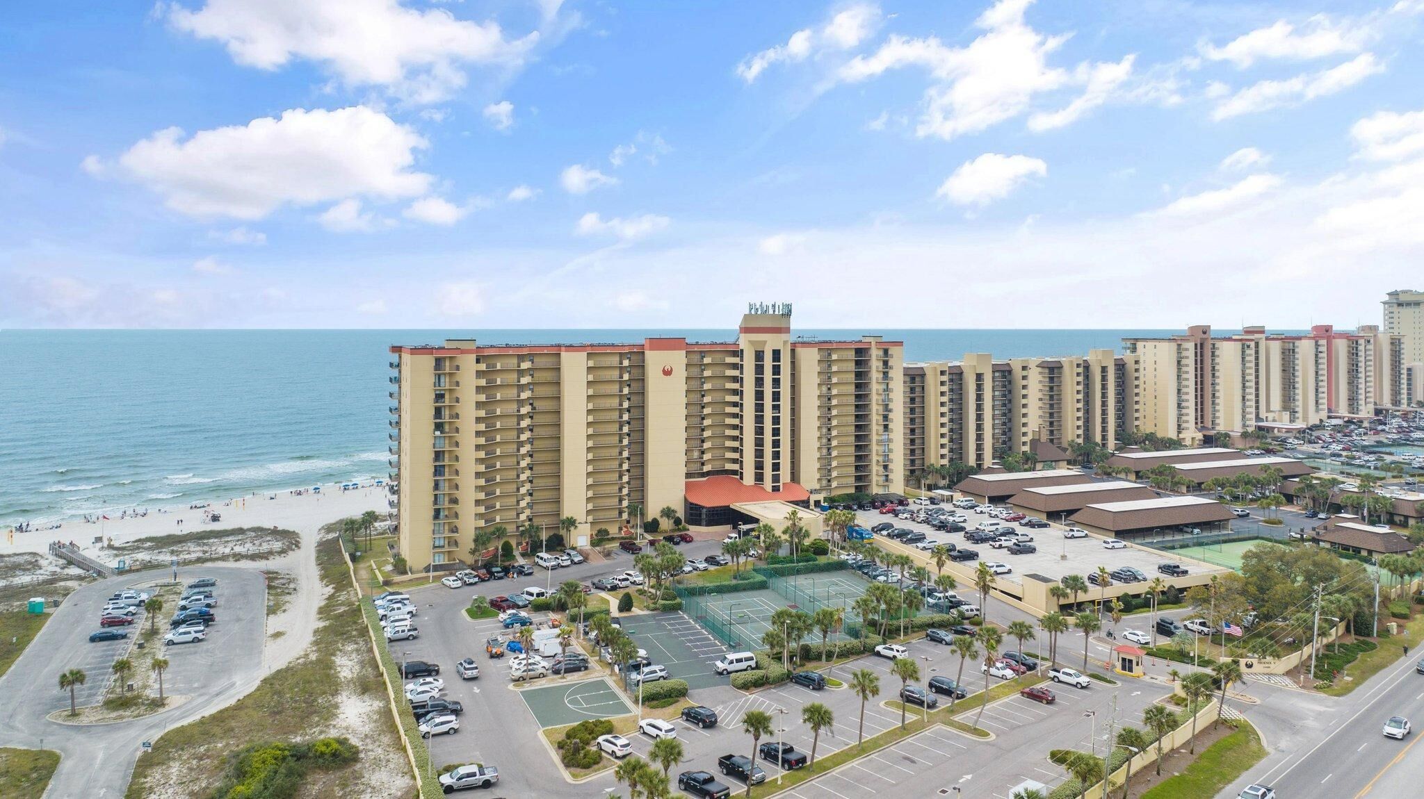 A coastal hotel with multiple high-rise buildings, a parking lot, and a beach area.