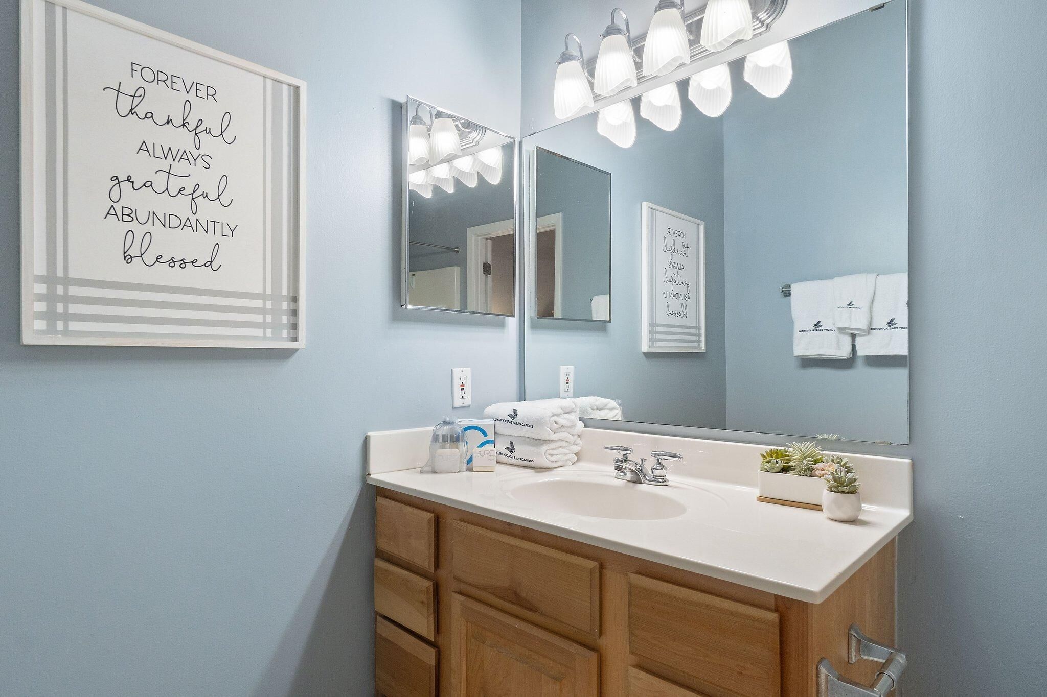 Un baño moderno con tocador blanco, dos lavamanos, un espejo grande y un aplique de pared.