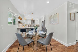 A modern kitchen with white cabinets, a central island, and a dining area with a round table and grey chairs. - The Fairy Tale Estate (Oceanside)