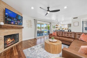 A modern living room with a fireplace, leather sofa, and a flat-screen TV mounted on a brick wall. - The Fairy Tale Estate (Oceanside)