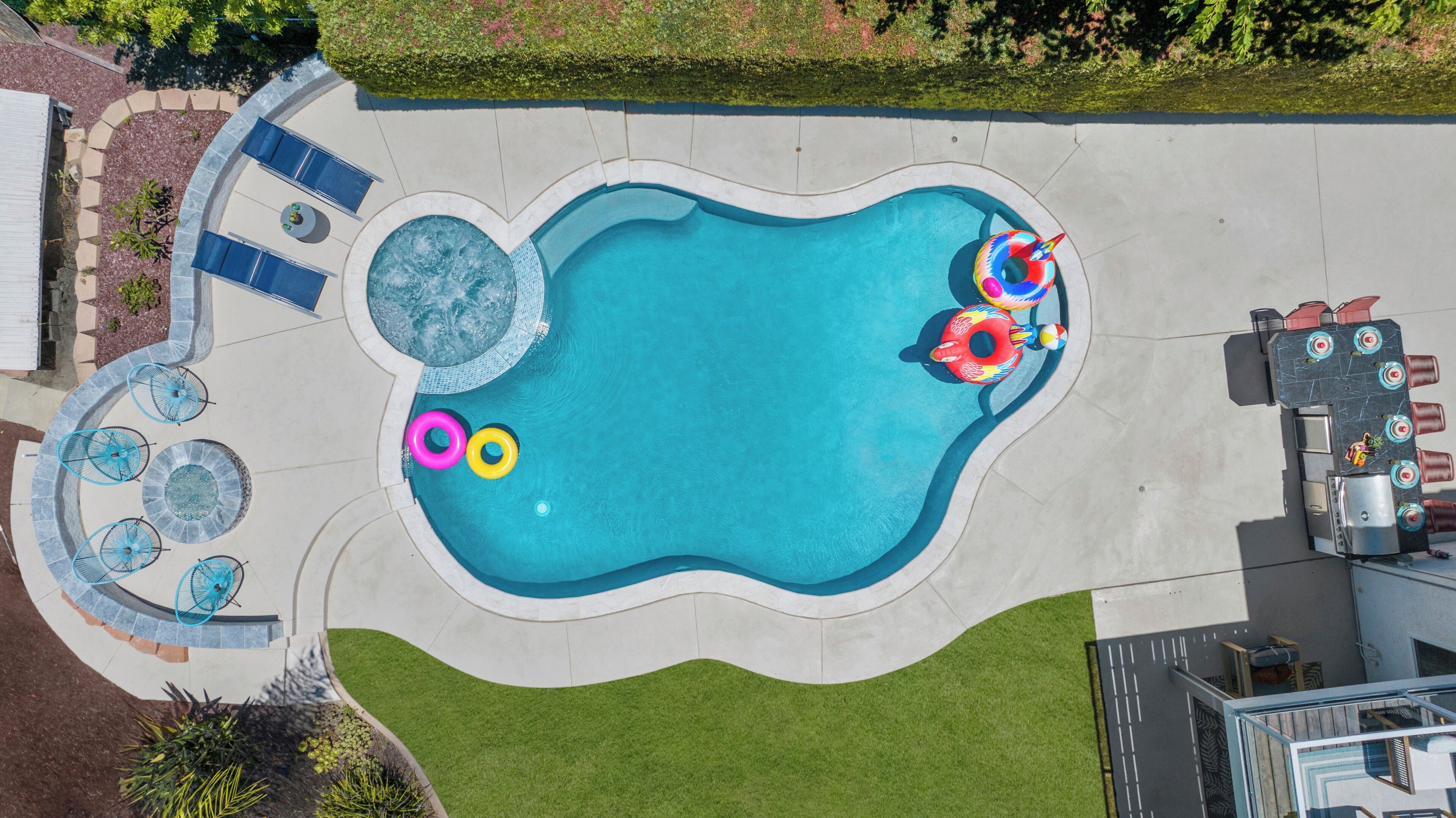 A swimming pool with a hot tub, lounge chairs, and inflatable toys.