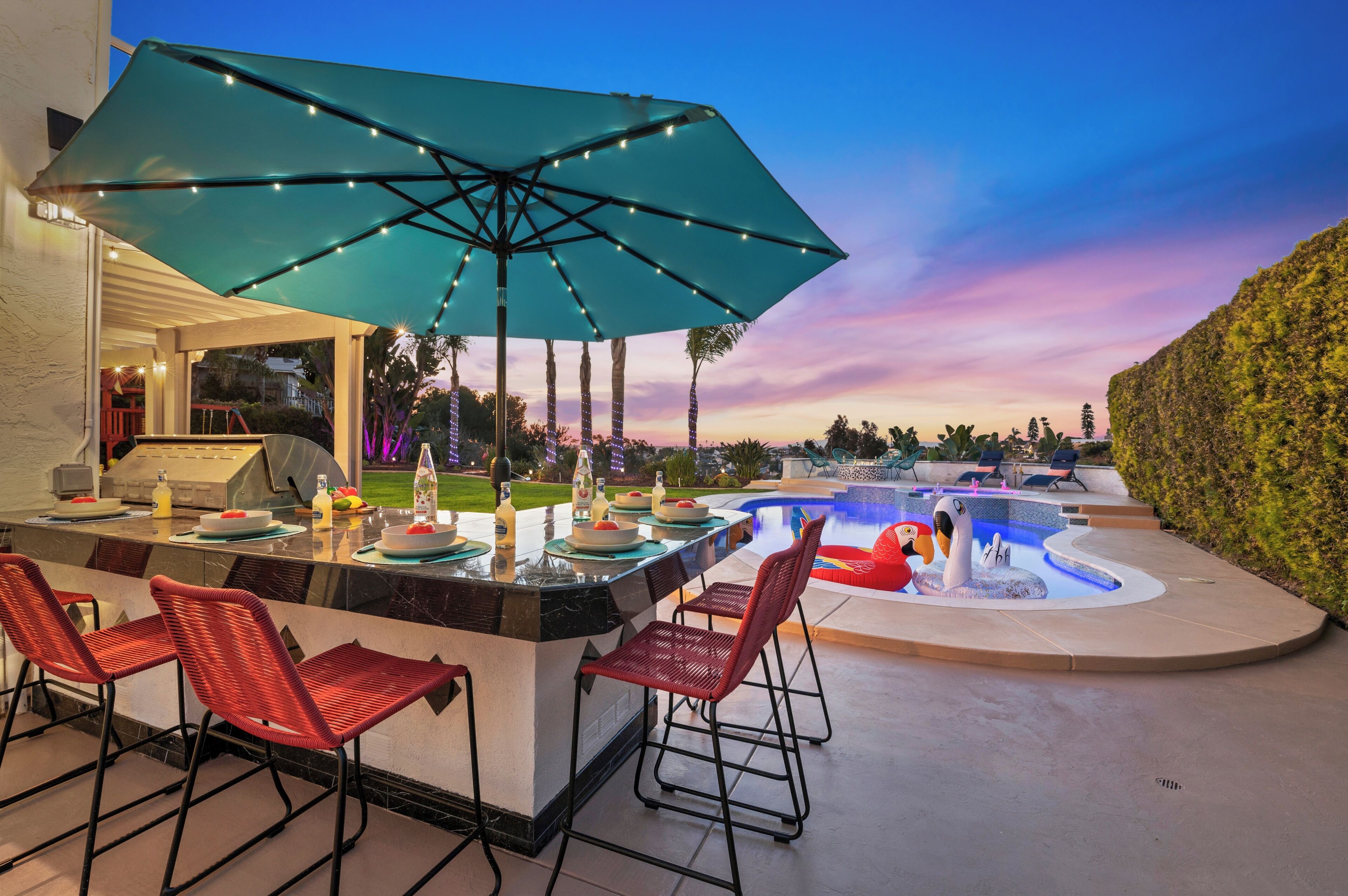 An outdoor bar area with a pool, red chairs, and a large umbrella.