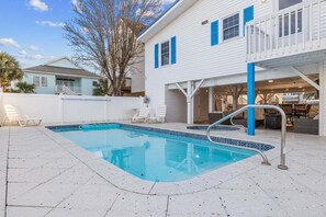 A swimming pool with a metal ladder, white lounge chairs, and a covered patio area.