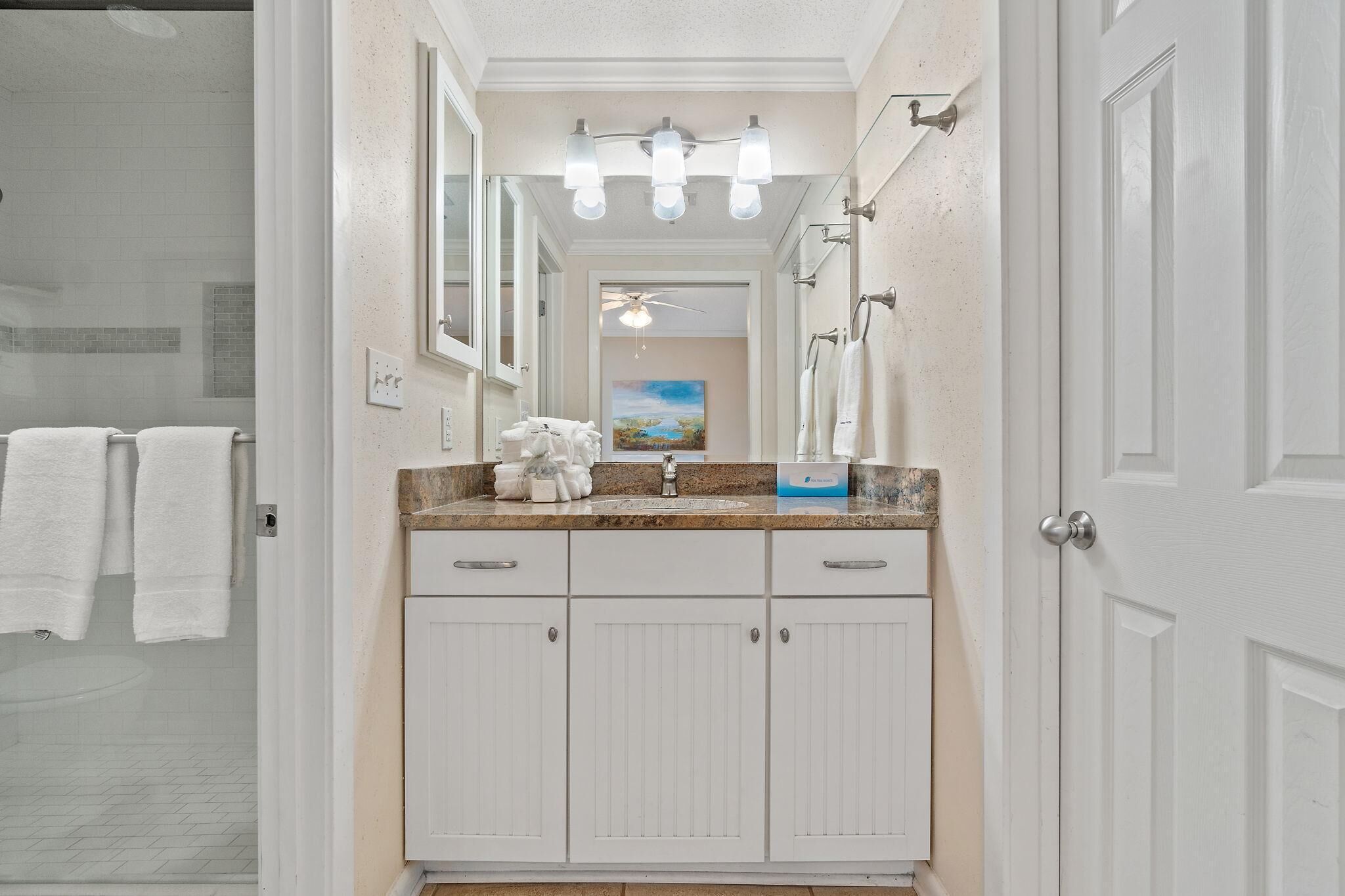 A bathroom with a double vanity, white cabinets, a granite countertop, a mirror, and a ceiling fan.