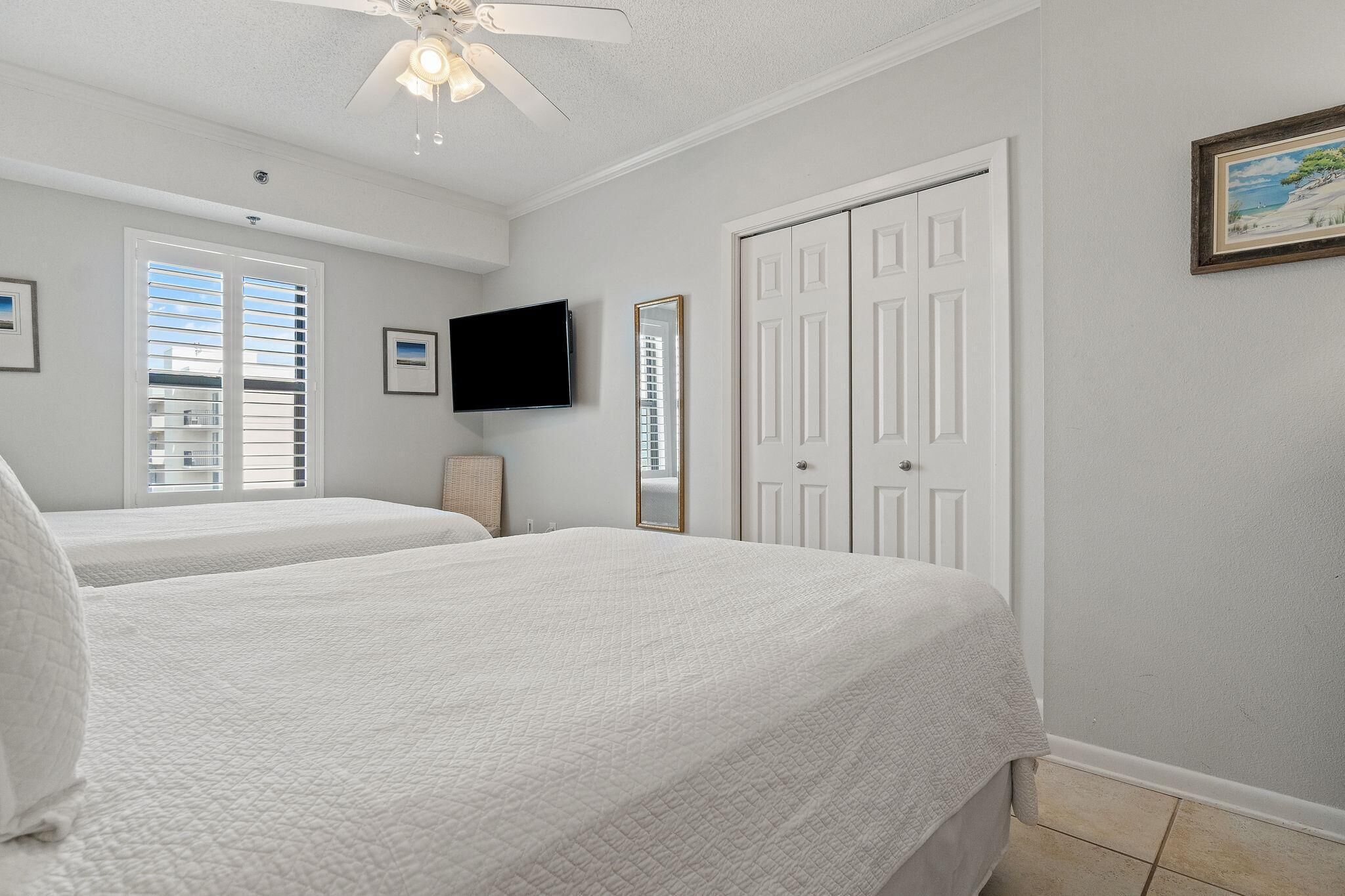 A bedroom with two beds, a ceiling fan, a TV, a mirror, and a door.