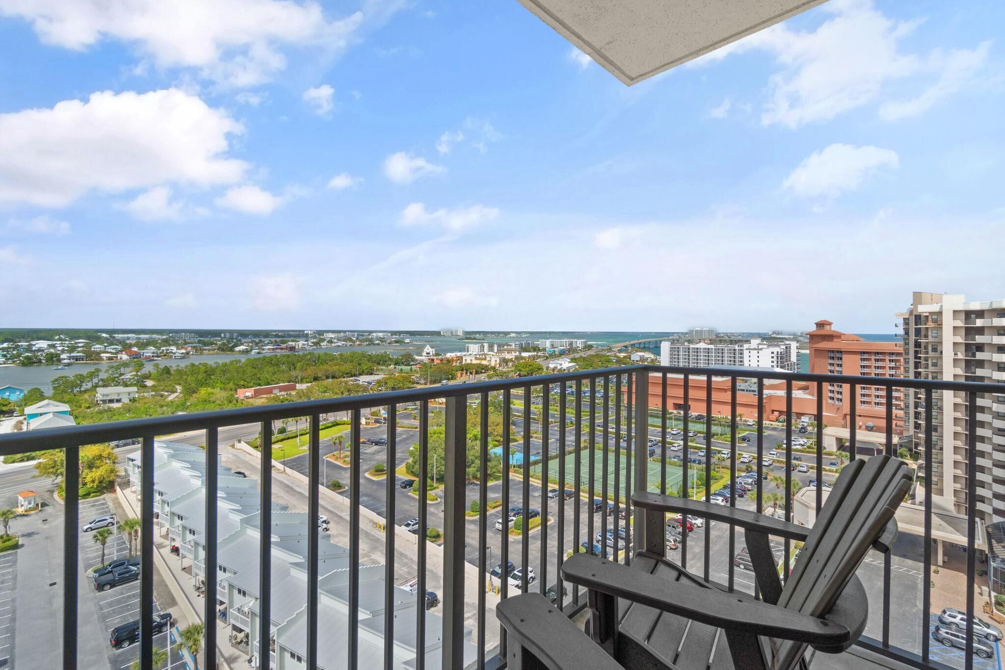Ein Balkon mit Blick auf eine Stadtlandschaft, darunter Gebäude und ein Parkplatz.
