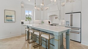 A modern kitchen with a large island, white cabinetry, and stainless steel appliances. - Battery 17 (Orange Beach)