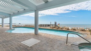 A pool area with a view of the ocean, a covered patio, and lounge chairs. - Colonnades 1601 (Gulf Shores)