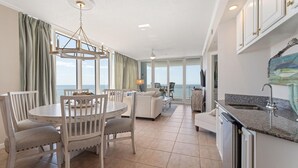 A spacious living area with a dining table, chairs, and a view of the ocean. - Colonnades 1601 (Gulf Shores)