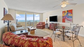 A spacious living room with a sofa, coffee table, TV, and dining area with chairs and a glass table. - Perdido Sun 610 (Pensacola)