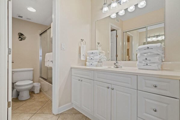 A bathroom with a white vanity, a large mirror, and a stack of towels.