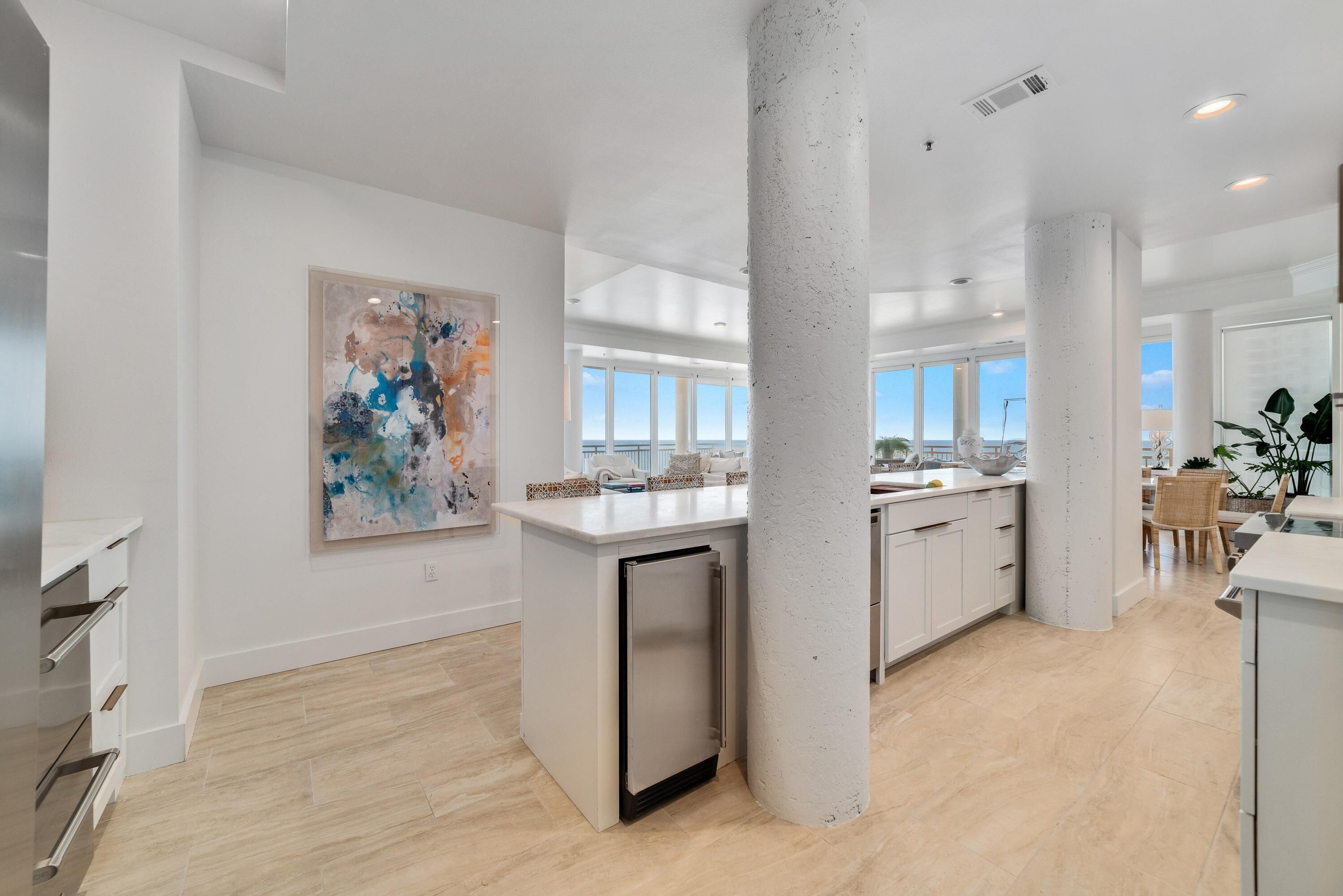A spacious kitchen with a central island, white cabinetry, and a large window providing a view of the outdoors.